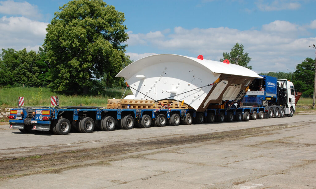 Długa naczepa modułowa Faymonville MODULE MAX w układzie wielu linii osiowych (do 21 osi) transportująca wielkogabarytowy element maszyny TBM do drążenia kolejowych tuneli w Łodzi. Widok z profilu na pełny zestaw transportowy Peterstar.